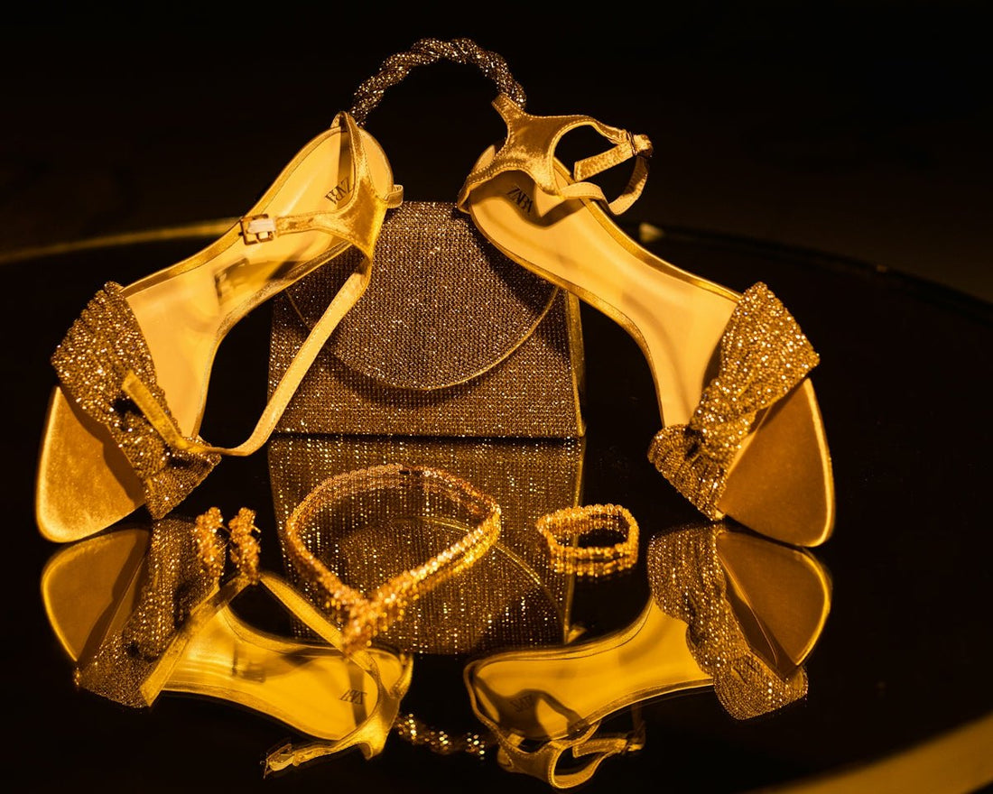 Golden high heels, handbag, and jewelry on a reflective surface