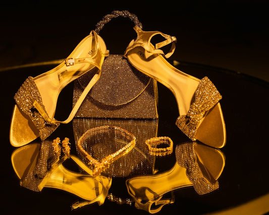 Golden high heels, handbag, and jewelry on a reflective surface