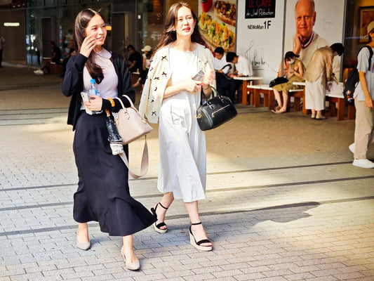 Two women walk together on a sunny street.