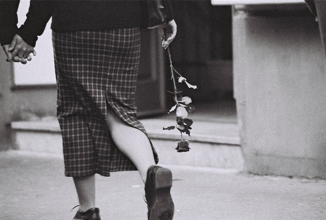 A person holds a rose and another's hand.