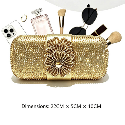 A gold rhinestone-covered clutch bag with a large floral embellishment on the front, shown holding makeup brushes, sunglasses, a perfume bottle, and a phone. Text at the bottom shows dimensions '22CM x 5CM x 10CM'.