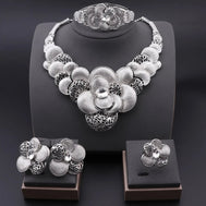 Silver floral jewelry set including necklace, bracelet, ring, and earrings on a dark background