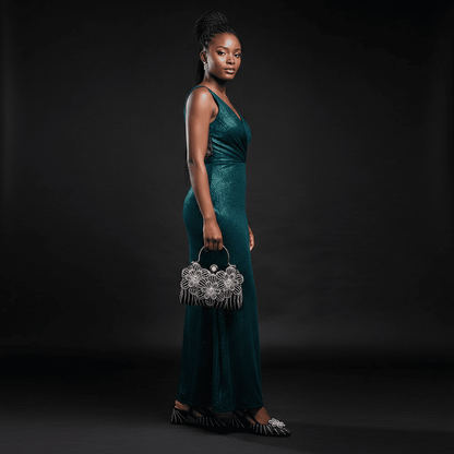 A model in a green dress, wearing a black Italian Rhinestone Heels and holding a matching black clutch bag against a black background