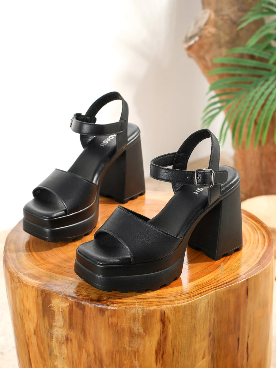 Black platform sandals on a wooden block with a plant in the background