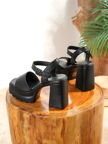 Black platform sandals on a wooden block with a blurred natural background