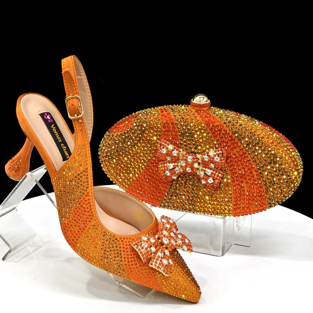 Orange high-heeled shoes with crystal embellishments and a matching clutch bag on a clear stand.