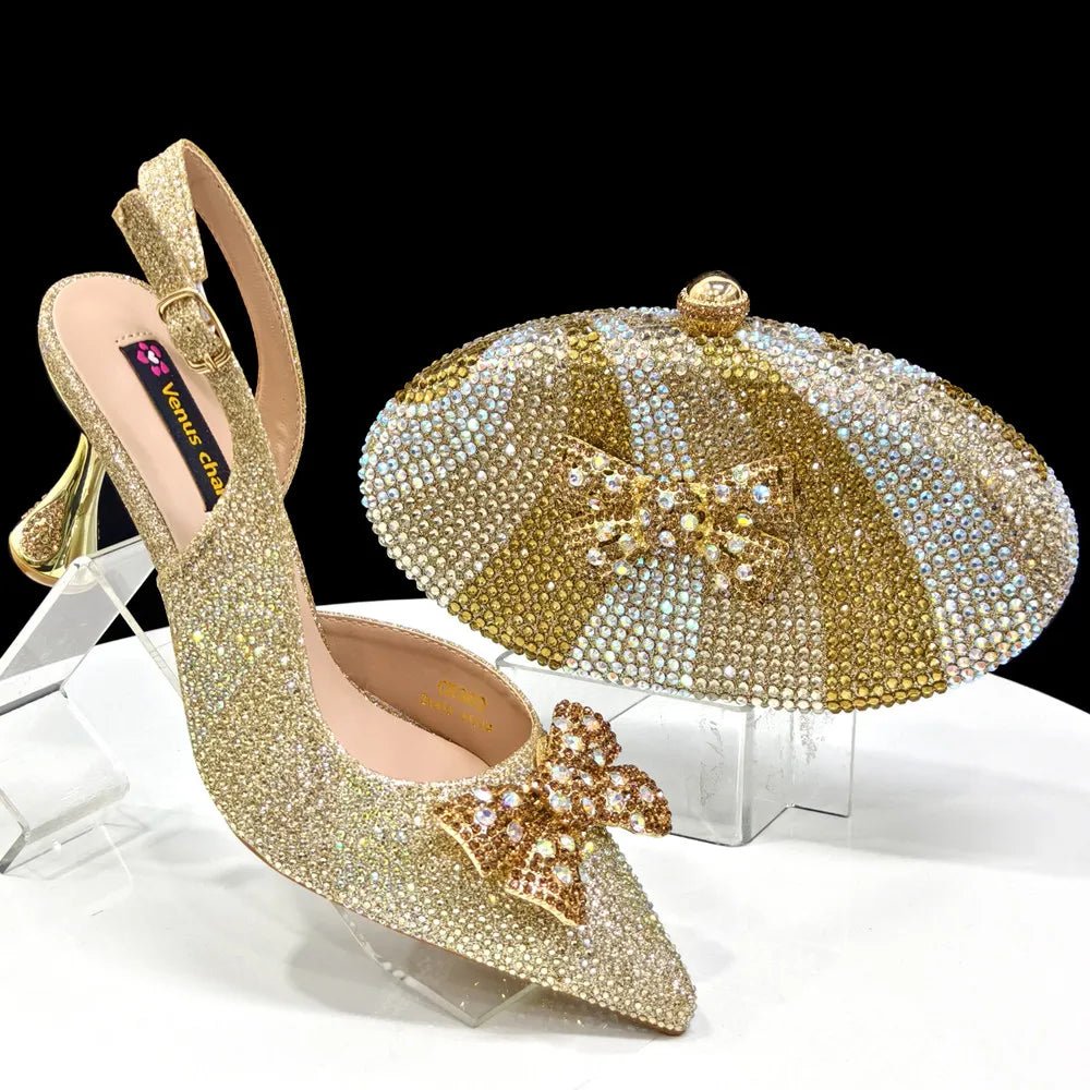 Gold high-heeled shoe with decorative bow and matching clutch bag on a clear stand.